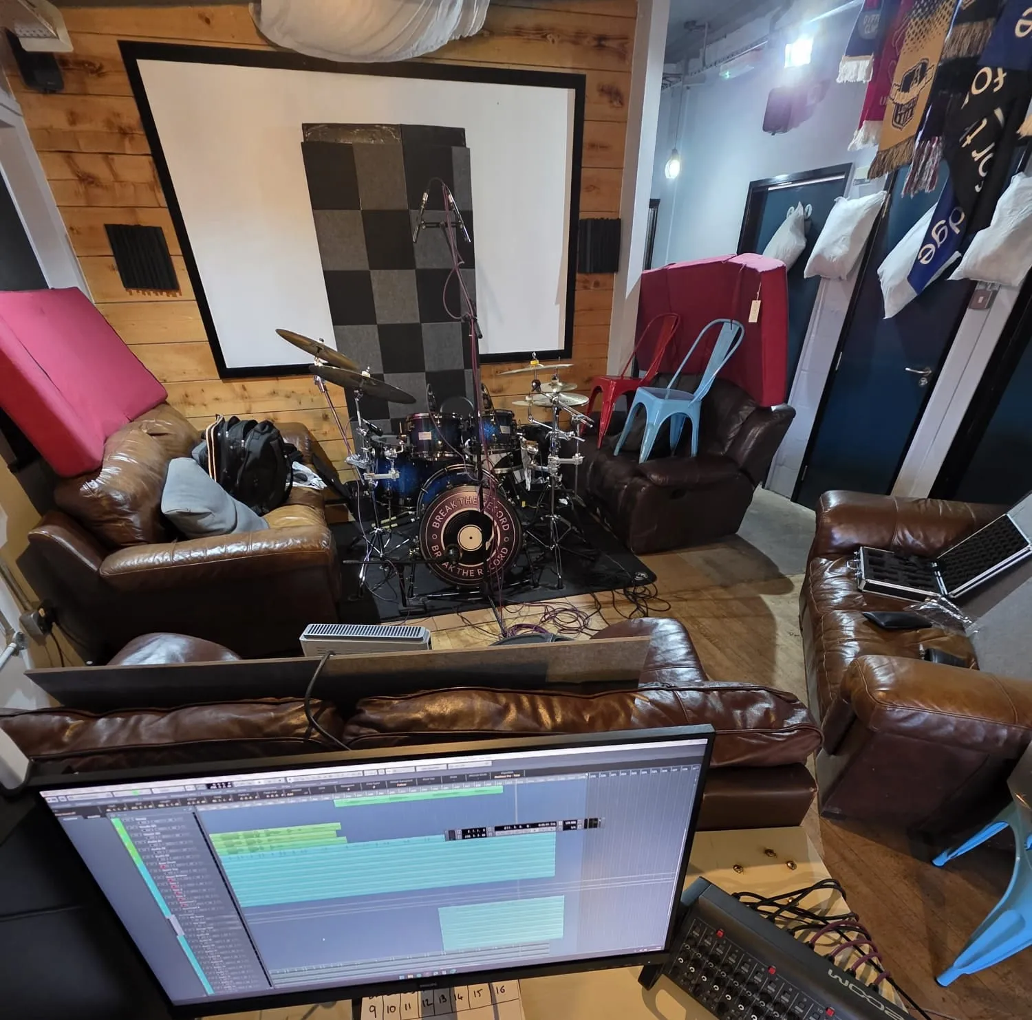 A home studio with a drum kit set up among guitars, a leather sofa and a laptop running a recording session.